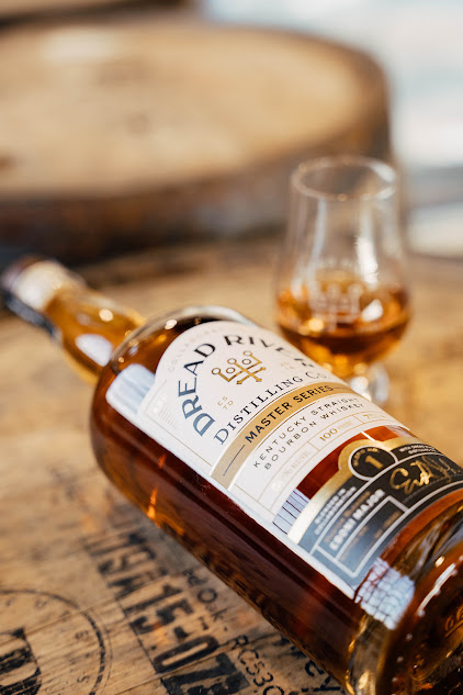 A bottle of Dread River Distilling Company’s Kentucky Straight Bourbon Whiskey resting on a barrel with a small glass of whiskey nearby.