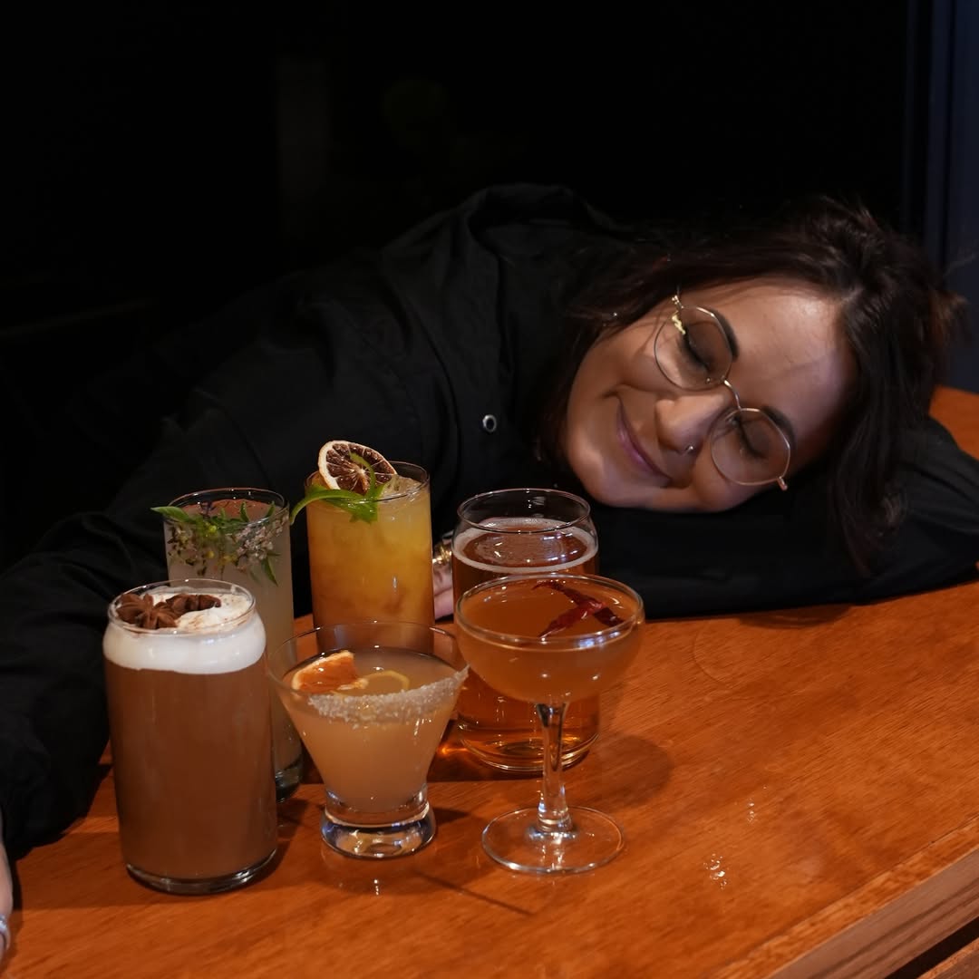 A woman resting on the bar beside a lineup of craft whiskey cocktails at Dread River Distilling Co.
