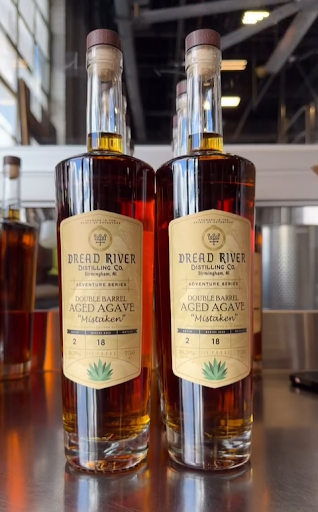 Two bottles of Dread River Distilling Co.'s Double Barrel Aged Agave 'Mistaken' placed on a distillery countertop, highlighting the rich amber color and distinctive label.