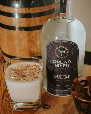 Dread River whiskey bottle served beside a creamy cocktail with oak barrels in the background.
