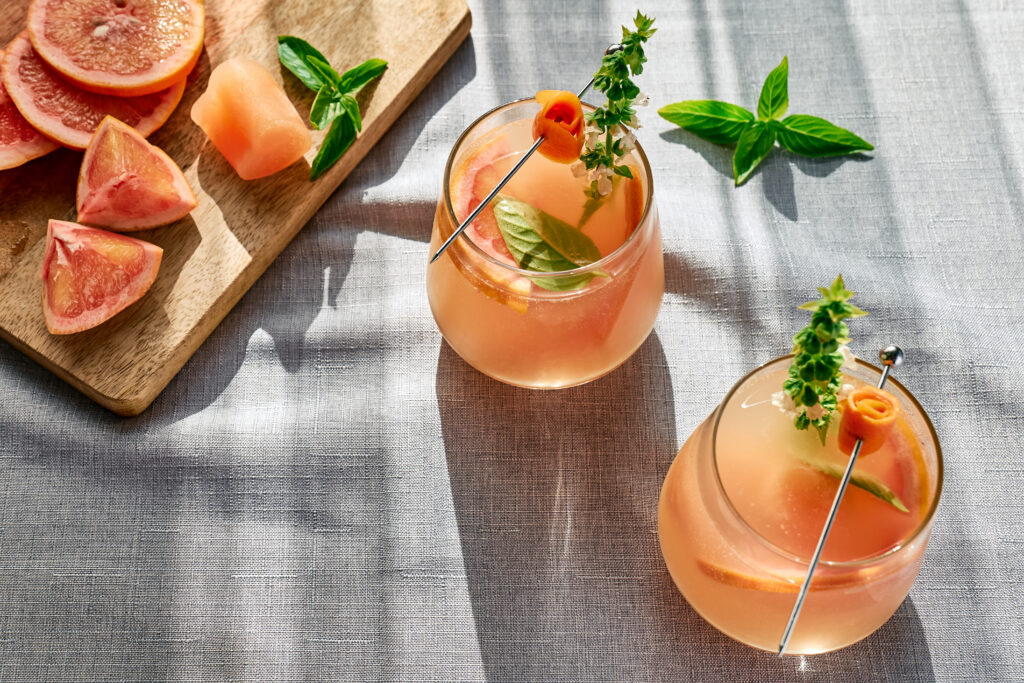 Summer refreshing grapefruit drink or alcoholic cocktail with grapefruit slices, ice and herbs. Citrus detox drink.