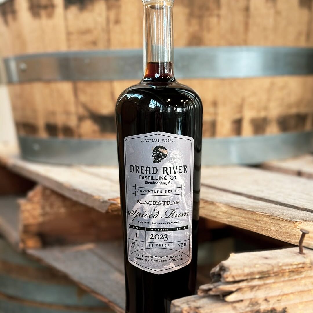 Close-up shot of a bottle of Blackstrap Spiced Rum from Dread River against a barrel and a wooden table.