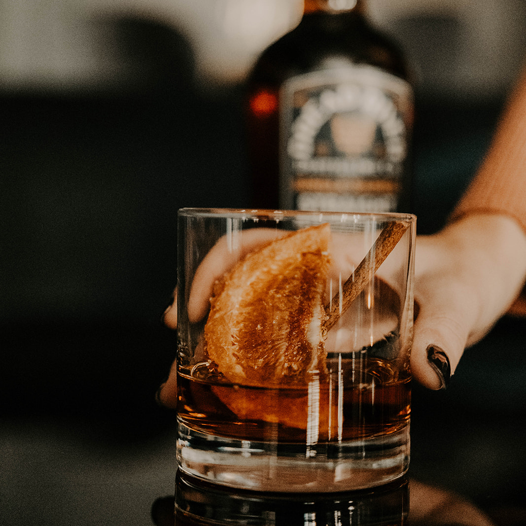 Hand holding a glass of whiskey from Dread River Distilling Co., showcasing amber hues and oak-aged depth.