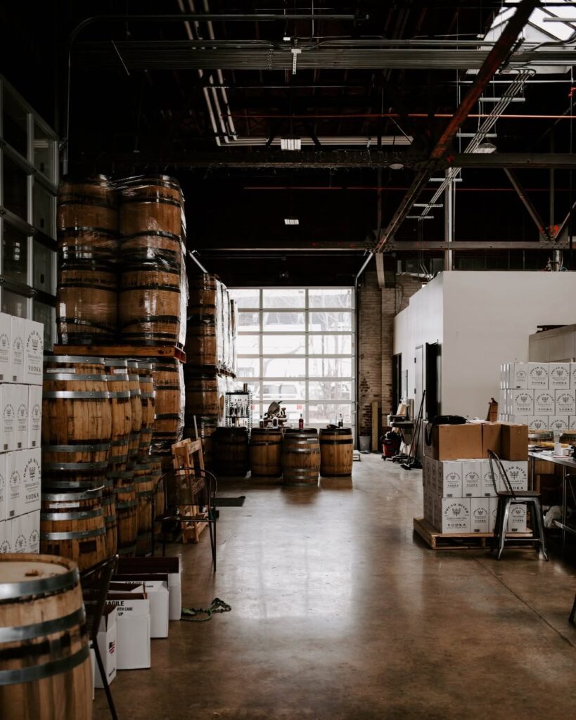 Inside Dread River Distilling Co.’s production area, showcasing rows of aging whiskey barrels and boxed spirits under moody lighting.