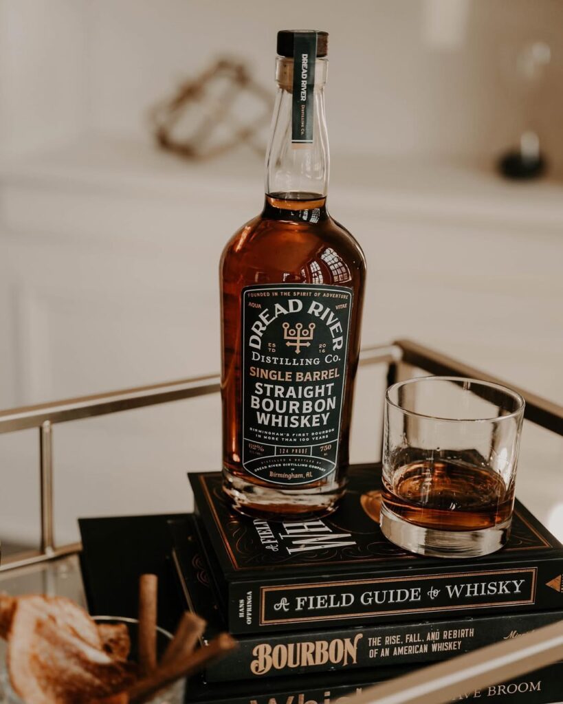 Dread River Single Barrel Straight Bourbon Whiskey with a rocks glass, styled on vintage whiskey books for a rich, classic cocktail setup.