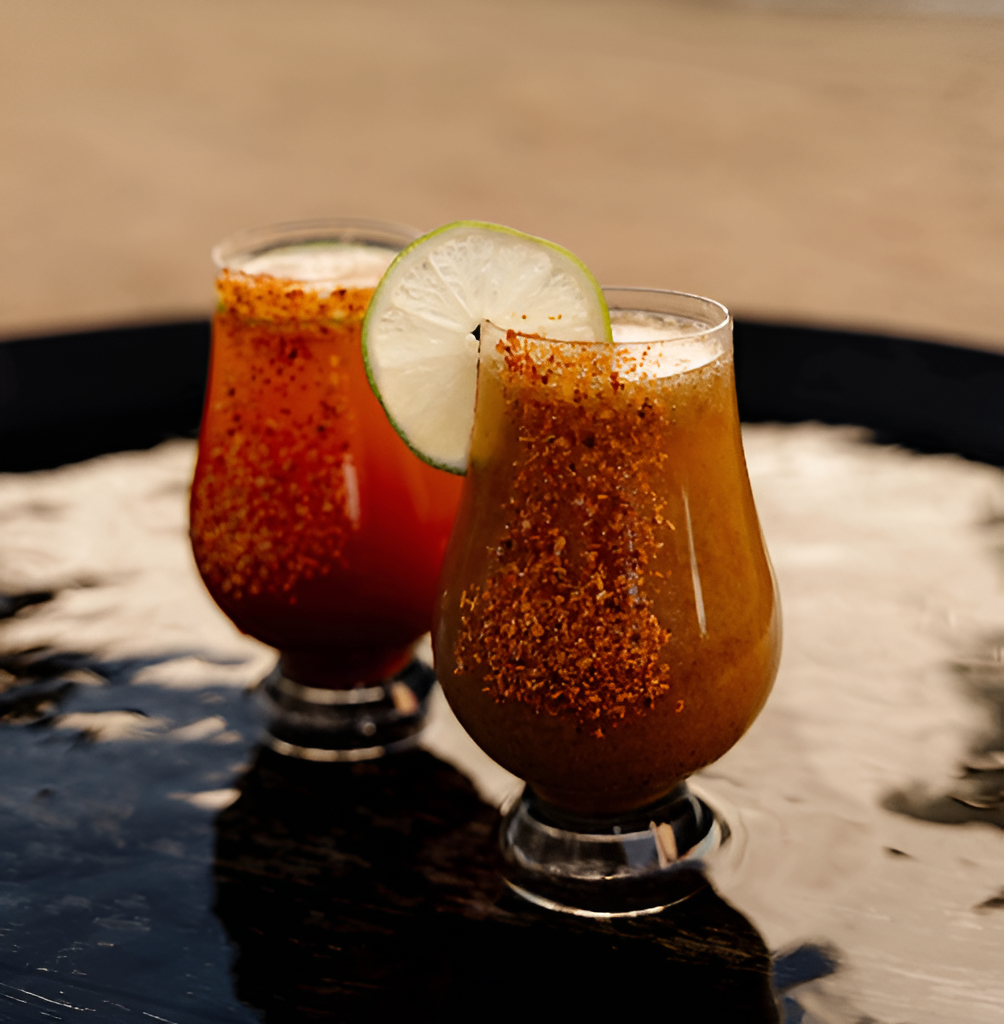 Two chili-rimmed tequila cocktails with lime garnish on a black table at Dread River, served in tulip glasses.