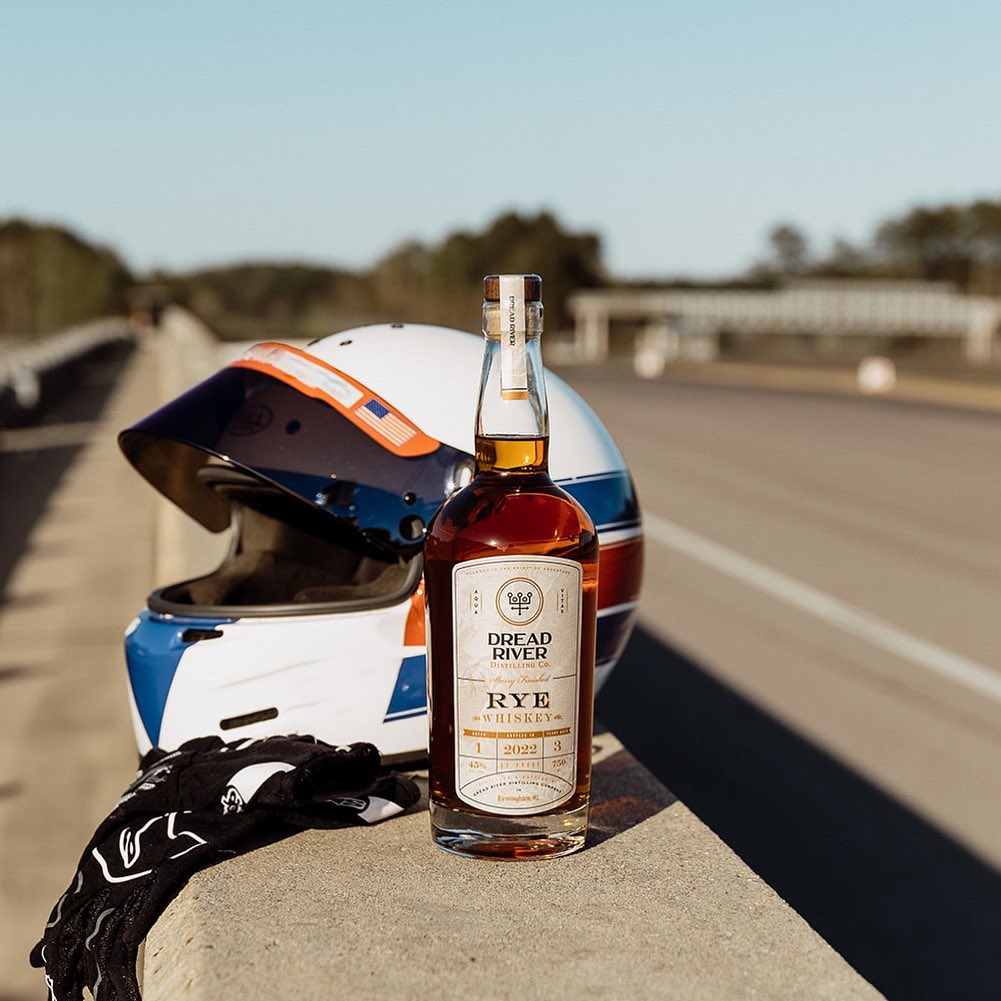 A bottle of Rye Whiskey from Dread River Distilling Co beside a bike helmet and gloves by the roadside.