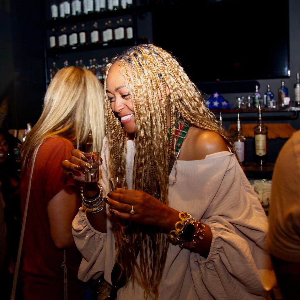 A guest smiling while holding two tasting shots at the Dread River Distilling Company bar.