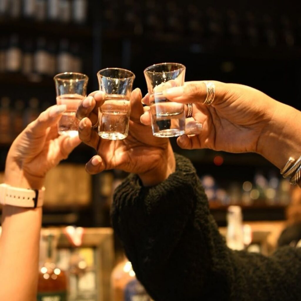 Hands raising three whiskey tasting glasses during a tasting at Dread River Distilling Company.