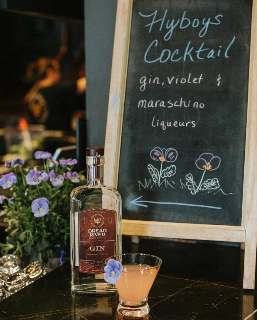 Dread River gin bottle displayed next to a chalkboard cocktail menu and a finished gin cocktail at the bar.