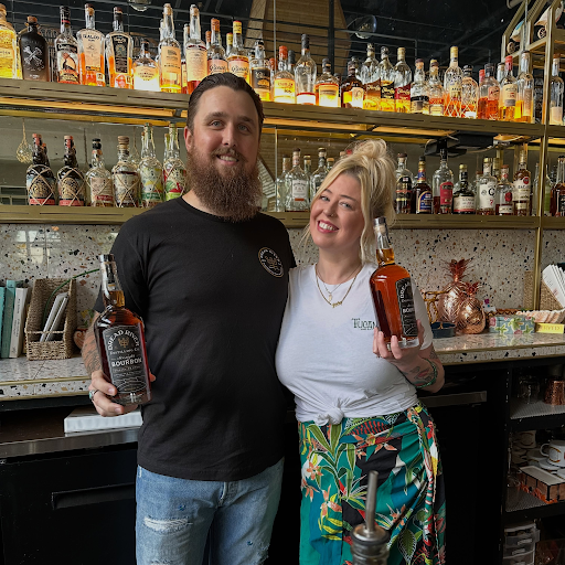 Dread River bourbon bottles raised in a toast behind a lively bar, showcasing Birmingham’s craft spirits scene and small-batch distilling.