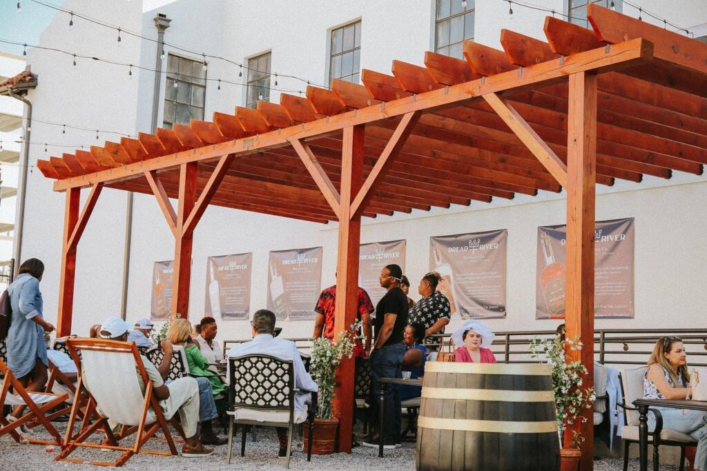 Guests gathering beneath a wooden pergola on the outdoor patio at Dread River Distilling Co.