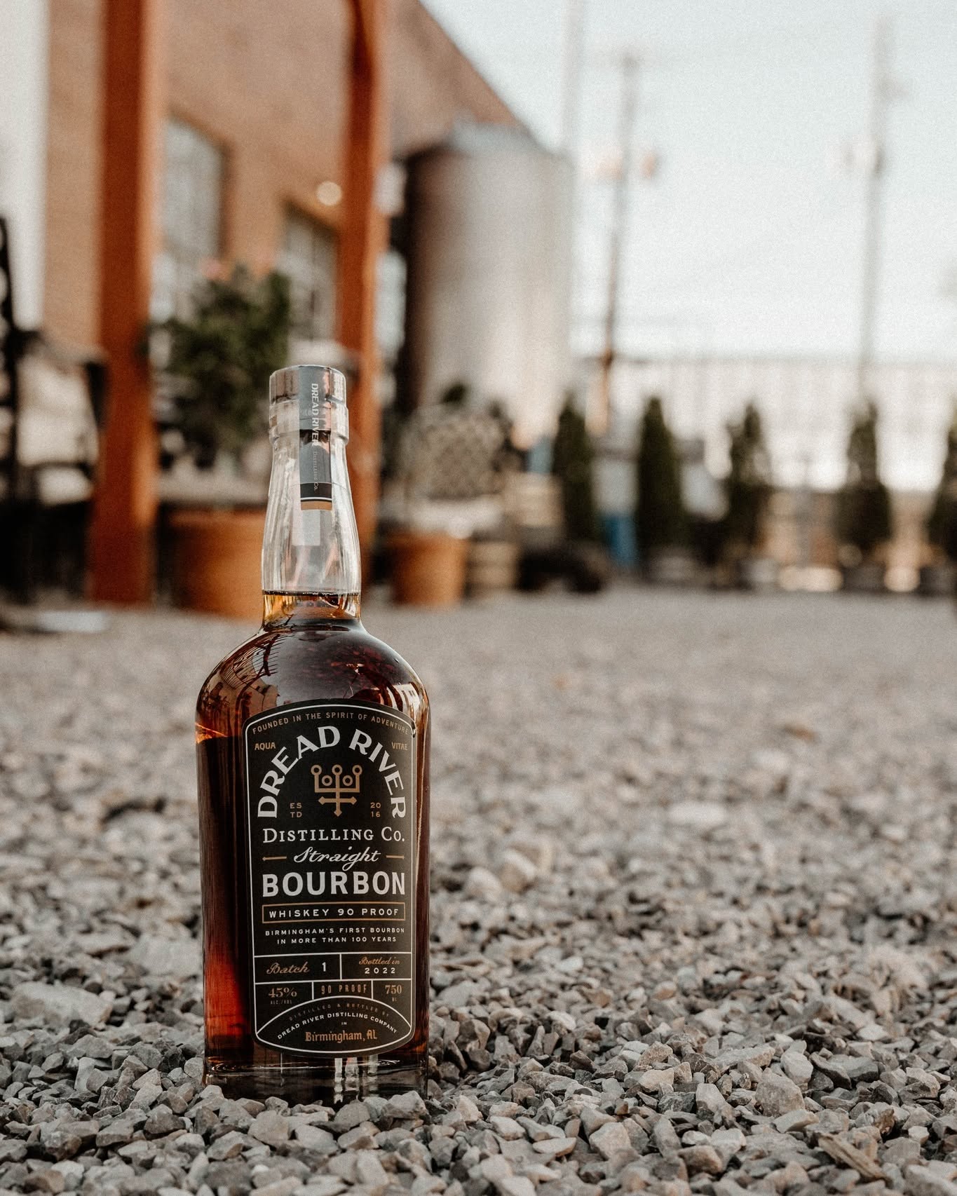 Dread River Straight Bourbon Whiskey bottle displayed on gravel outside the distillery.
