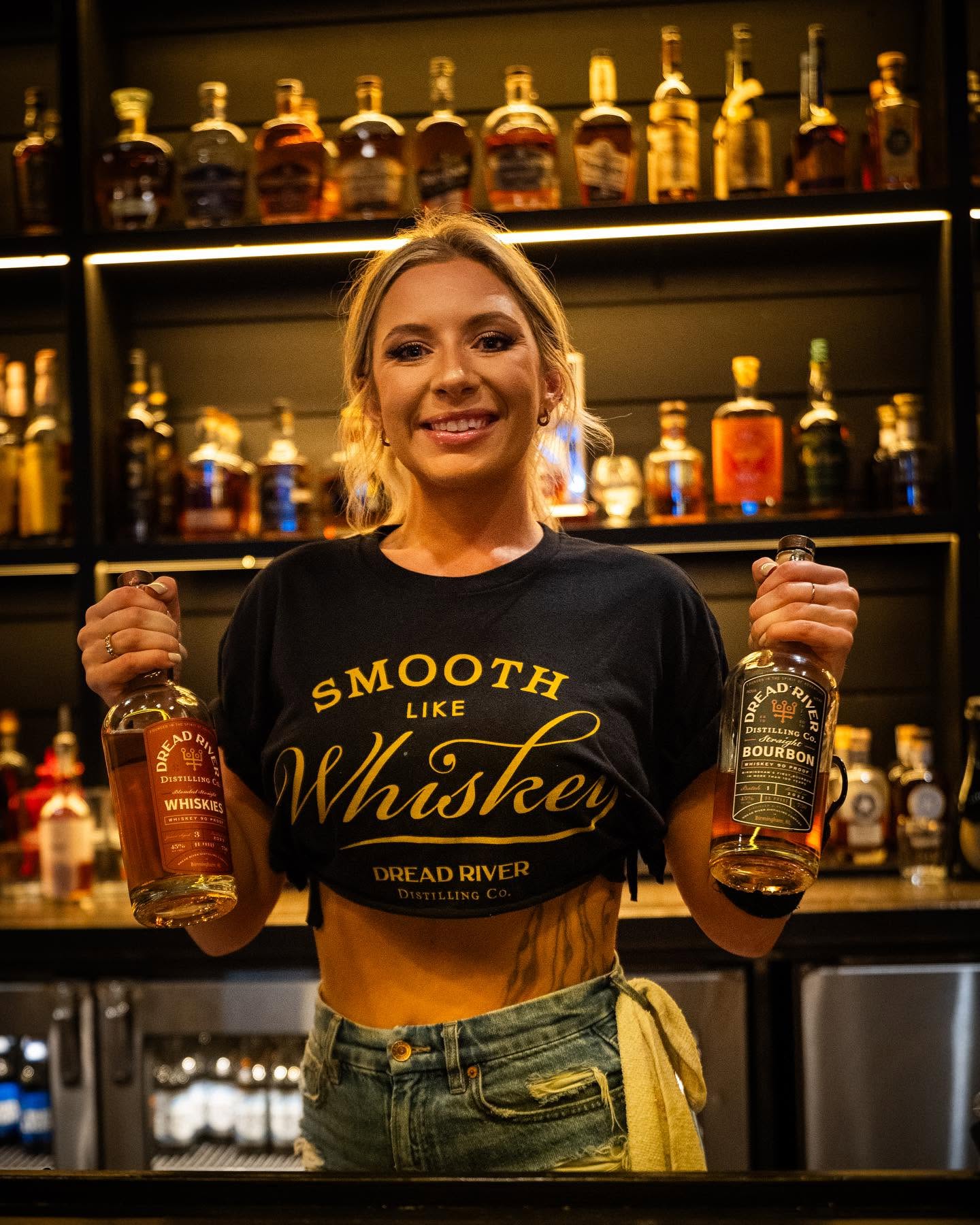 Dread River bartender holding bottles of bourbon and blended whiskey behind the bar.