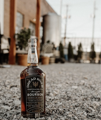 Dread River bourbon bottle placed on gravel outside the distillery with a blurred building background.