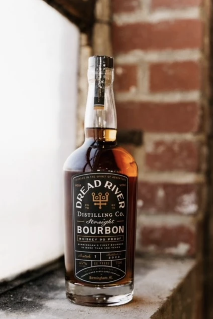 Dread River bourbon bottle placed on gravel outside the distillery with a blurred building background.