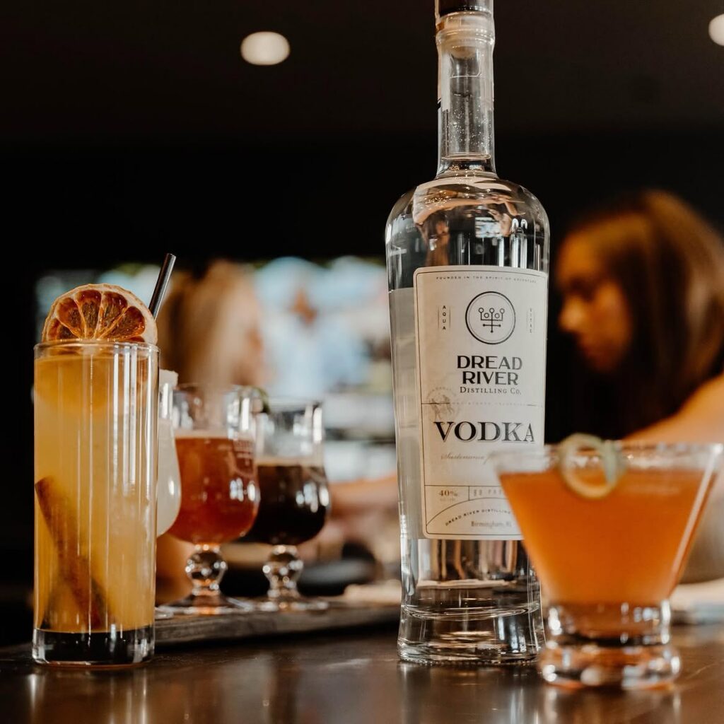 Dread River vodka bottle displayed on a bar with crafted cocktails and a warm distillery lounge atmosphere.