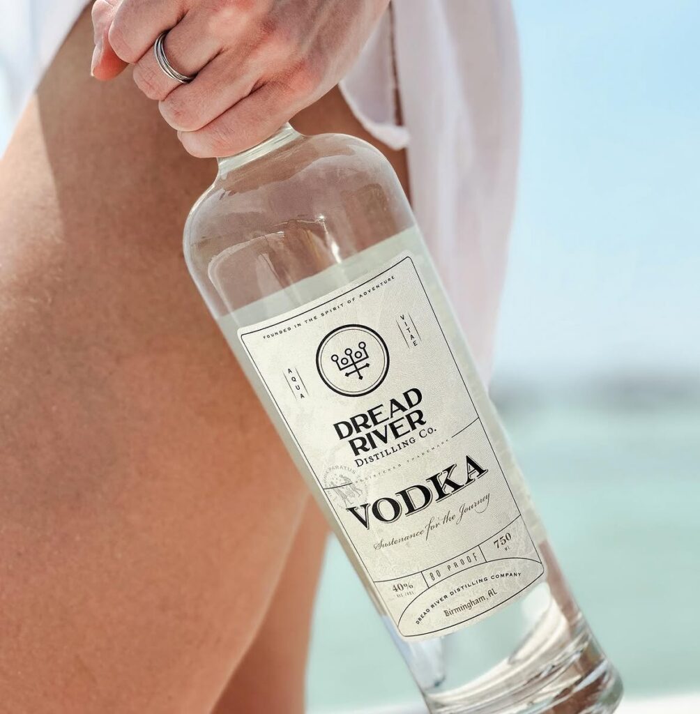 Dread River vodka bottle held outdoors near a pool with a bright, summery lifestyle backdrop.